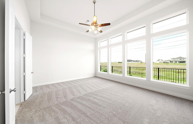 carpeted empty room with baseboards, ceiling fan, visible vents, and a raised ceiling