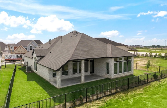 back of property with a lawn, brick siding, a patio area, and roof with shingles