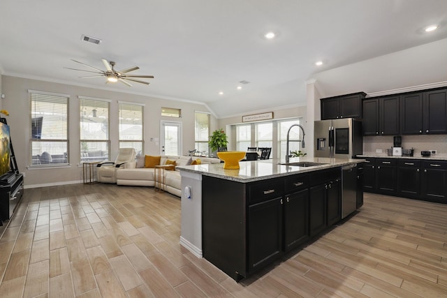 kitchen with light wood-type flooring, appliances with stainless steel finishes, sink, and an island with sink