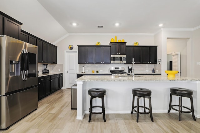 kitchen featuring a kitchen island with sink, vaulted ceiling, light wood-type flooring, a kitchen bar, and stainless steel appliances