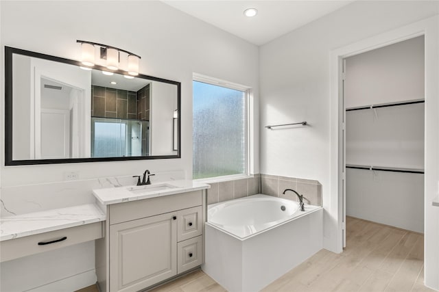 full bathroom with wood finished floors, a spacious closet, vanity, a shower stall, and a bath