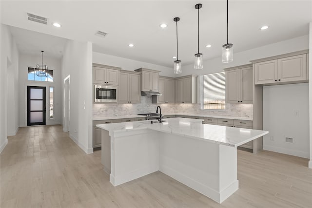 kitchen featuring built in microwave, a kitchen island with sink, visible vents, and light stone countertops