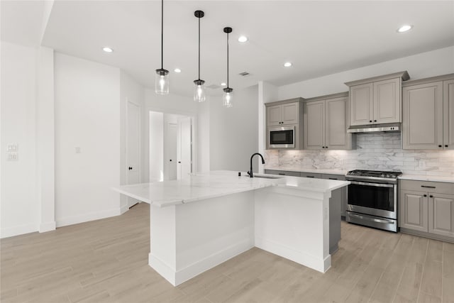 kitchen featuring a center island with sink, light stone counters, and appliances with stainless steel finishes