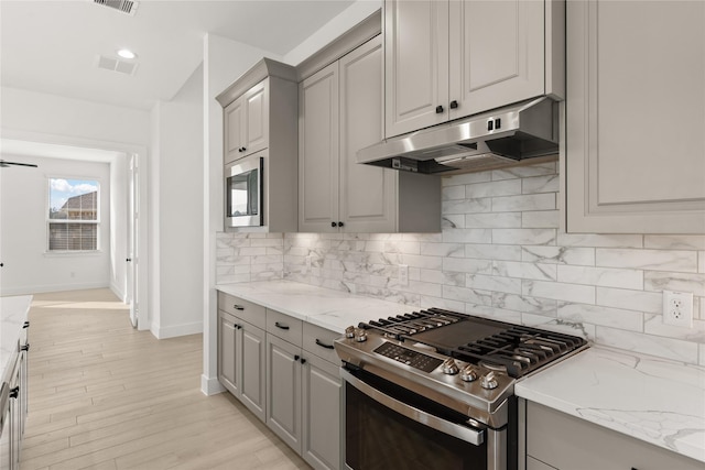 kitchen featuring gray cabinetry, built in microwave, stainless steel gas range, light stone counters, and backsplash