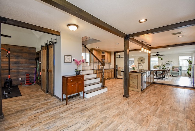 kitchen with dishwasher, light hardwood / wood-style flooring, ceiling fan, a barn door, and beam ceiling