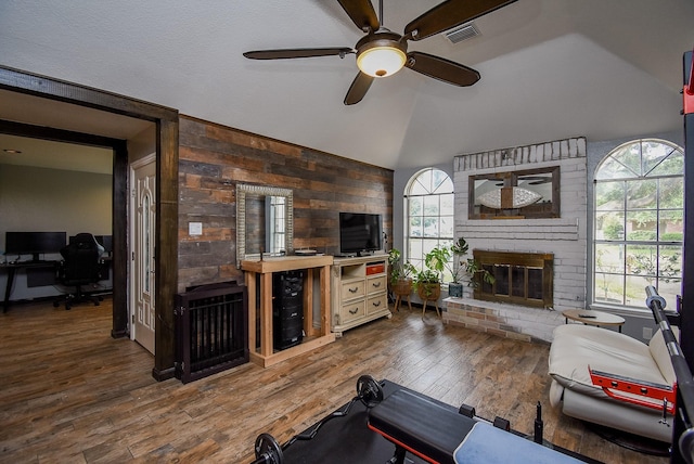 living room with wood-type flooring, vaulted ceiling, ceiling fan, and a brick fireplace