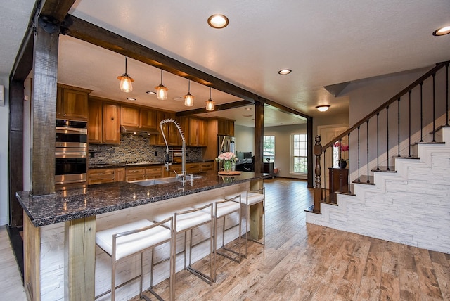 kitchen featuring dark stone countertops, beam ceiling, decorative light fixtures, light hardwood / wood-style floors, and a breakfast bar area