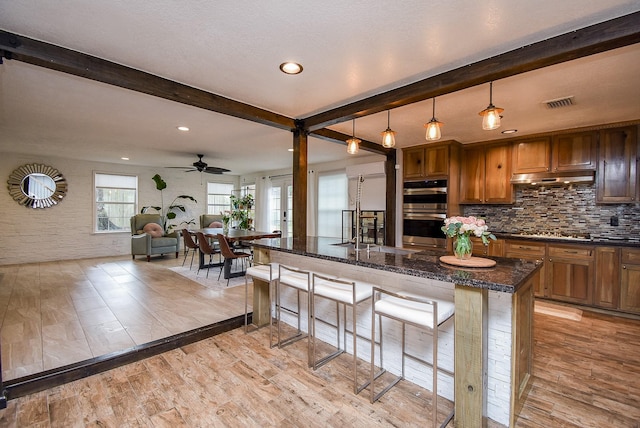 kitchen with a kitchen bar, beam ceiling, light wood-type flooring, and stainless steel double oven