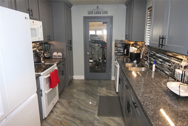 kitchen with dark stone countertops, white appliances, sink, and tasteful backsplash