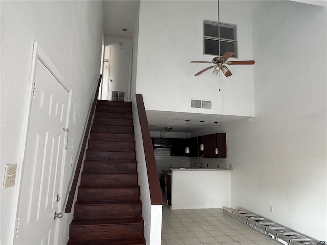 staircase with tile patterned flooring, ceiling fan, and a towering ceiling