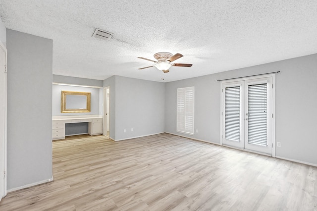 unfurnished living room featuring a textured ceiling, light wood-type flooring, ceiling fan, and built in desk