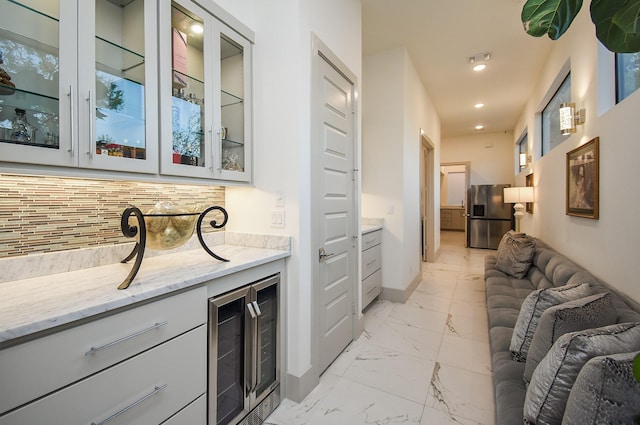 bar featuring decorative backsplash, light stone counters, stainless steel fridge with ice dispenser, and wine cooler