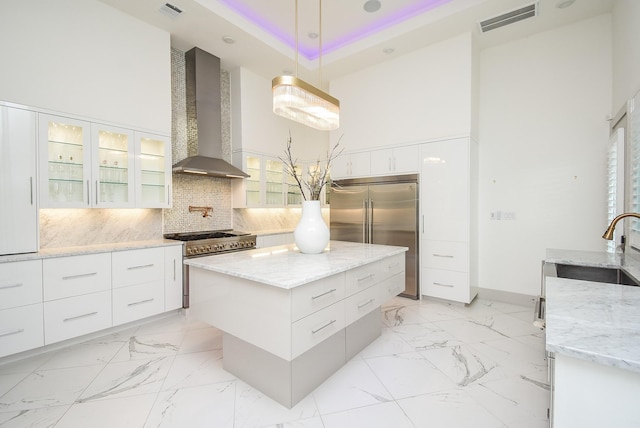 kitchen with high end appliances, wall chimney range hood, white cabinets, a kitchen island, and hanging light fixtures