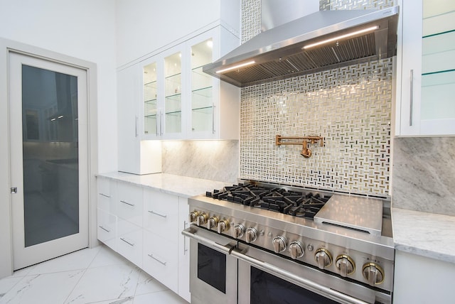 kitchen with tasteful backsplash, white cabinetry, wall chimney exhaust hood, and double oven range