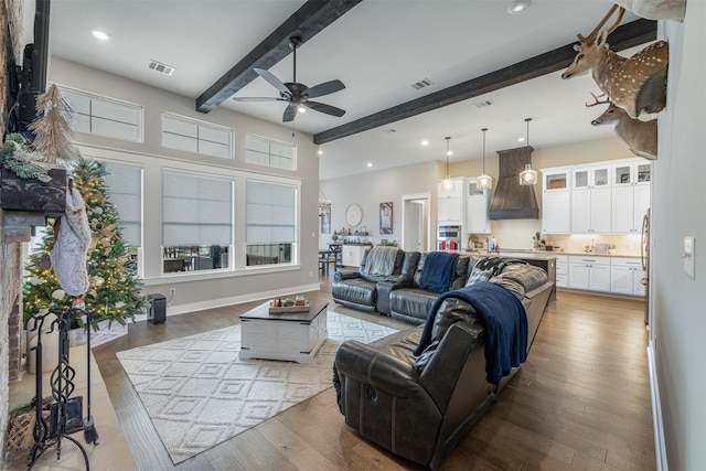 living room featuring ceiling fan, wood-type flooring, and beamed ceiling