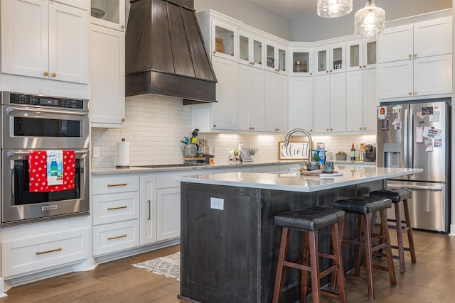 kitchen featuring appliances with stainless steel finishes, white cabinetry, a center island, custom range hood, and decorative light fixtures