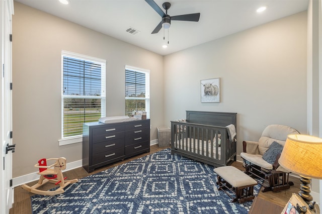 bedroom with dark wood-type flooring, ceiling fan, and a crib