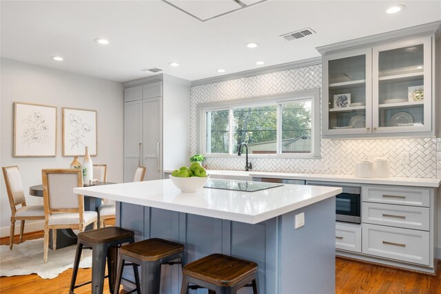 kitchen featuring built in microwave, tasteful backsplash, crown molding, light hardwood / wood-style floors, and a kitchen island