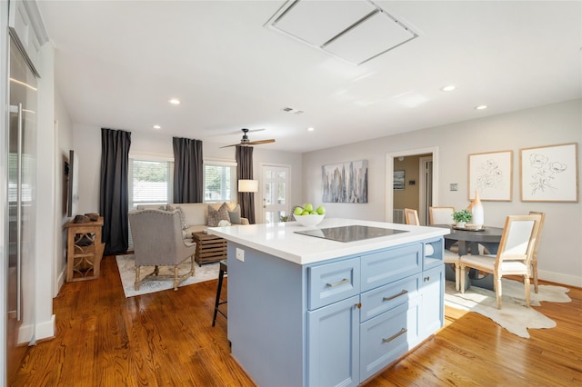 kitchen with ceiling fan, dark hardwood / wood-style floors, a kitchen bar, black electric stovetop, and a kitchen island