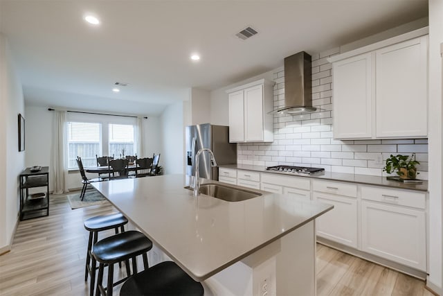 kitchen with a center island with sink, wall chimney exhaust hood, light wood-type flooring, and sink