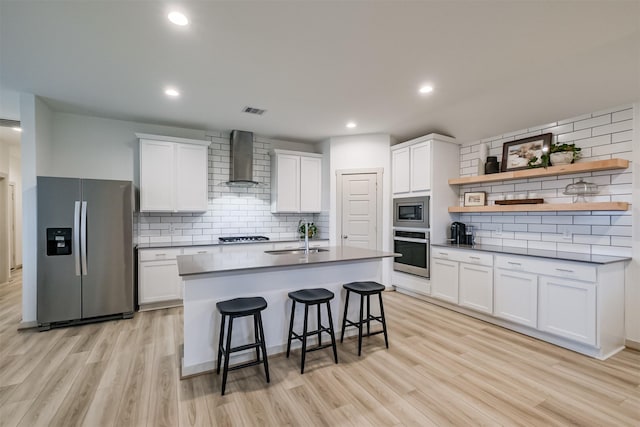 kitchen with appliances with stainless steel finishes, wall chimney exhaust hood, a breakfast bar, sink, and white cabinets