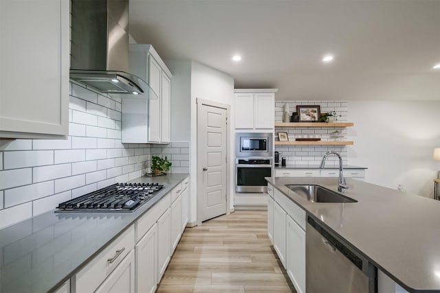 kitchen featuring white cabinets, wall chimney range hood, sink, light hardwood / wood-style flooring, and stainless steel appliances