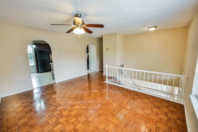 empty room with arched walkways, ceiling fan, and baseboards