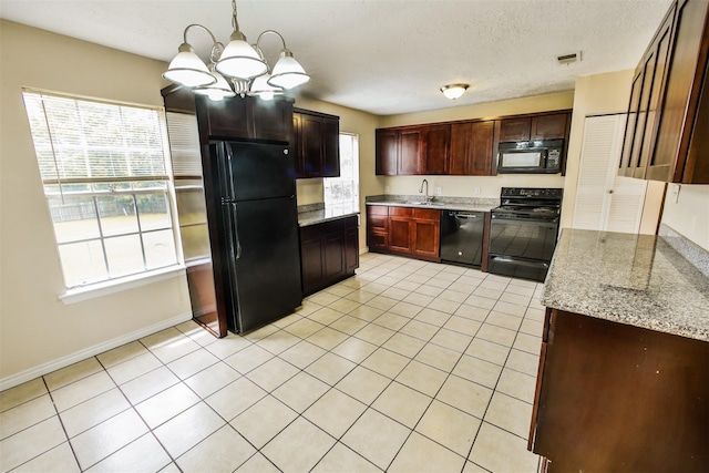 kitchen with light stone counters, visible vents, hanging light fixtures, a sink, and black appliances