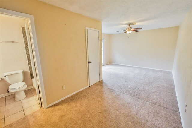 unfurnished room featuring light carpet, light tile patterned floors, a ceiling fan, and baseboards