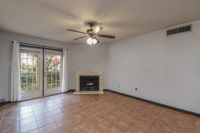 unfurnished living room with ceiling fan, a premium fireplace, a textured ceiling, and light tile patterned floors