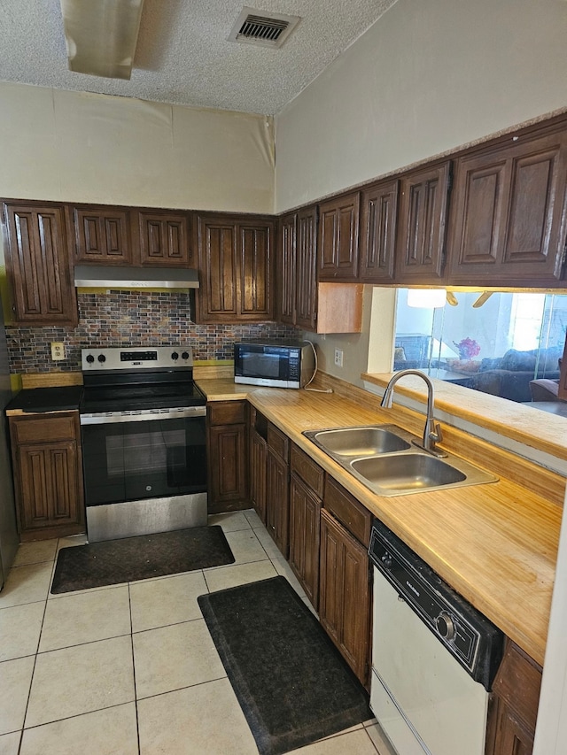 kitchen featuring sink, stainless steel appliances, backsplash, a textured ceiling, and light tile patterned floors