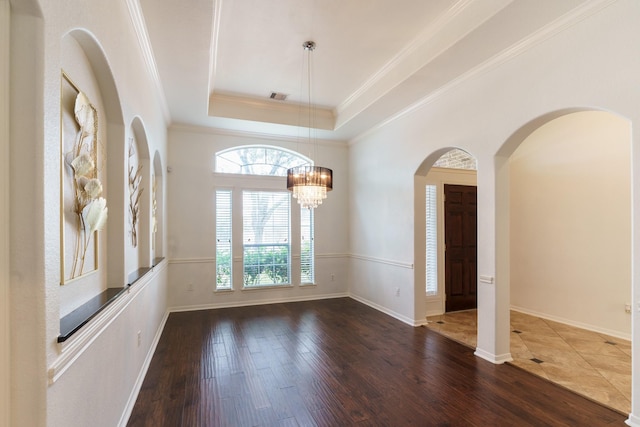 unfurnished room with ornamental molding, a tray ceiling, dark wood-type flooring, and a notable chandelier