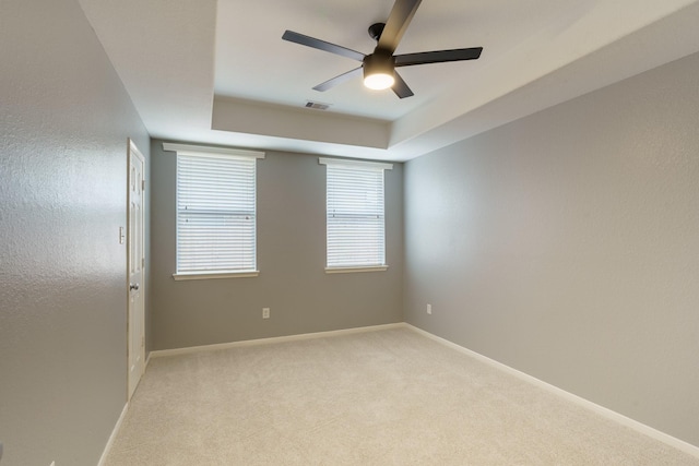 unfurnished room with a raised ceiling, ceiling fan, and light colored carpet