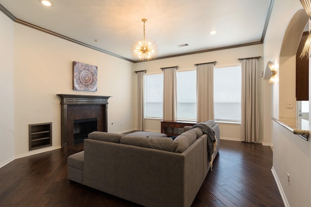 living room featuring a tile fireplace, crown molding, dark wood-type flooring, and a notable chandelier