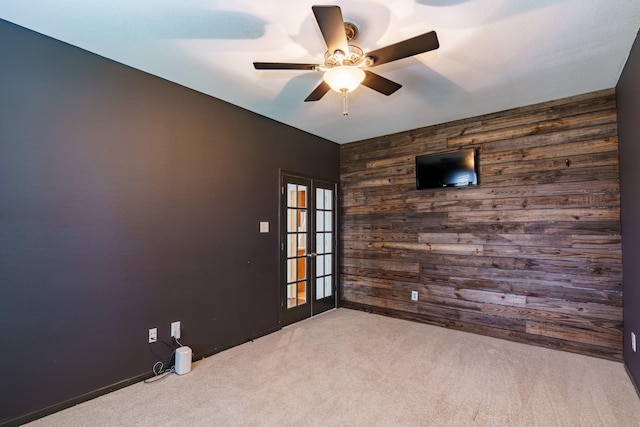 carpeted empty room featuring french doors, ceiling fan, and wooden walls