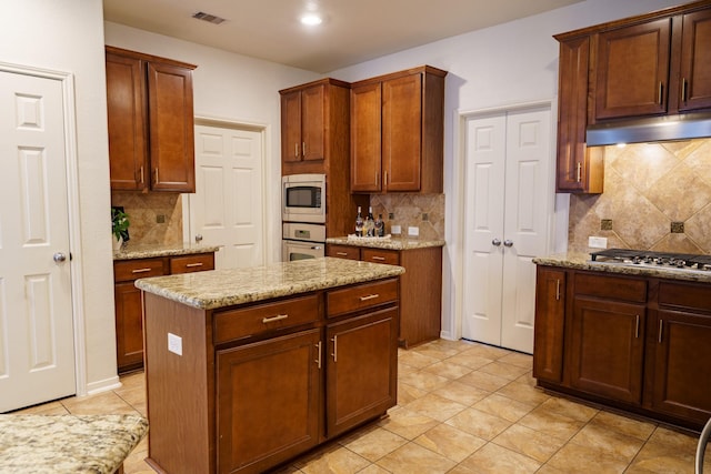 kitchen with tasteful backsplash, light stone counters, a center island, and stainless steel appliances