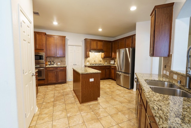 kitchen with a center island, stainless steel appliances, light stone counters, and sink