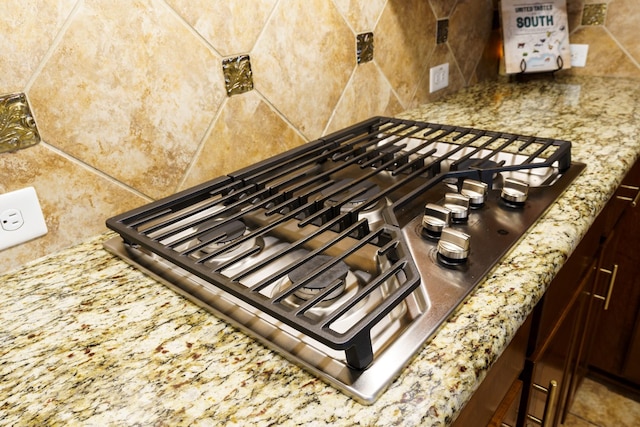 room details with decorative backsplash, light stone countertops, and stainless steel gas cooktop