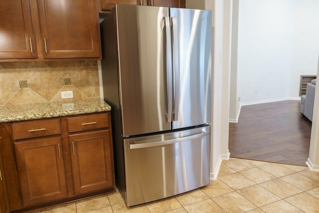 kitchen featuring tasteful backsplash, stainless steel fridge, light stone counters, and light wood-type flooring