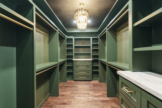 spacious closet featuring light hardwood / wood-style floors and an inviting chandelier