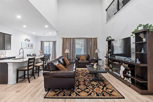 living room featuring a towering ceiling, light hardwood / wood-style floors, and sink