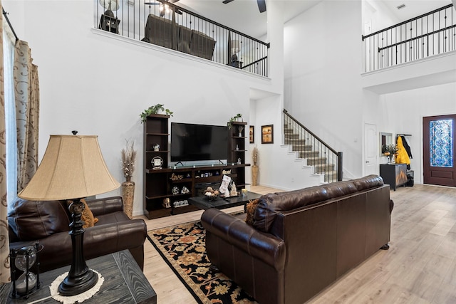 living room with a towering ceiling, light hardwood / wood-style floors, and ceiling fan