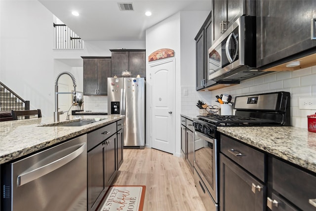 kitchen featuring light stone countertops, sink, stainless steel appliances, light hardwood / wood-style floors, and decorative backsplash