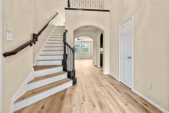 staircase with wood-type flooring, a towering ceiling, and ceiling fan