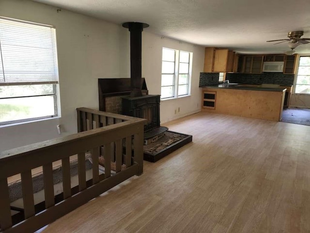 living room with ceiling fan, light hardwood / wood-style floors, and a wood stove