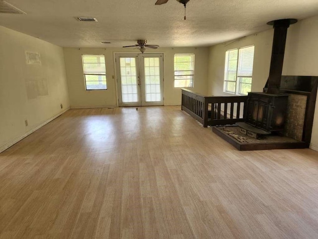 unfurnished living room with ceiling fan, a wood stove, a textured ceiling, and light hardwood / wood-style flooring