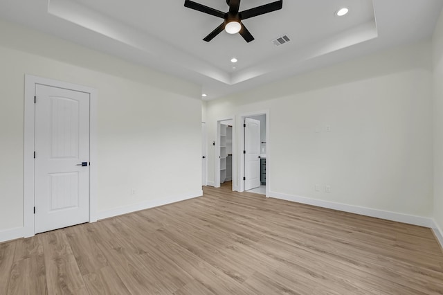 unfurnished bedroom featuring light hardwood / wood-style floors, ensuite bath, ceiling fan, and a tray ceiling