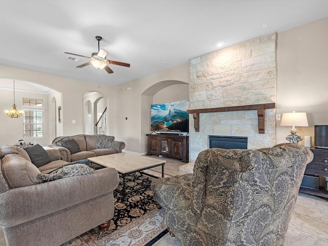 living room with ceiling fan with notable chandelier and a stone fireplace