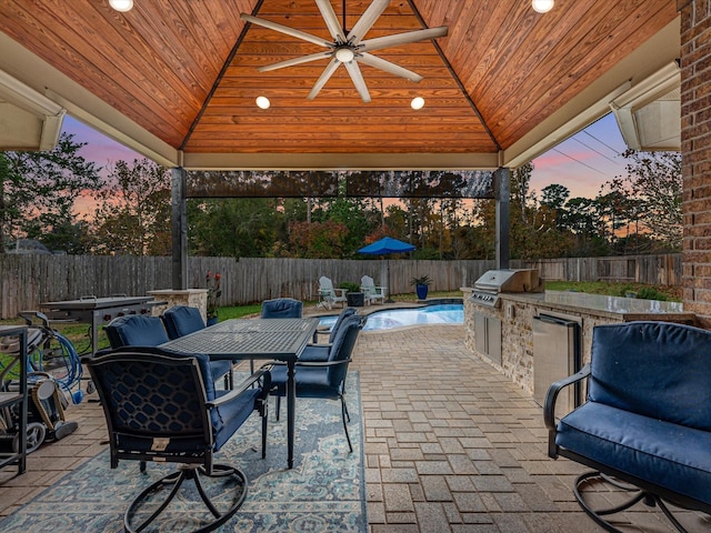 patio terrace at dusk featuring area for grilling, a gazebo, an outdoor kitchen, and ceiling fan