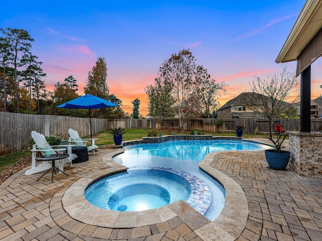 pool at dusk featuring an in ground hot tub and a patio area